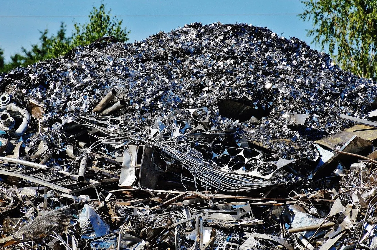Großer Haufen aus gemischtem Metallschrott mit Rohren, Drähten und Blechteilen unter blauem Himmel.