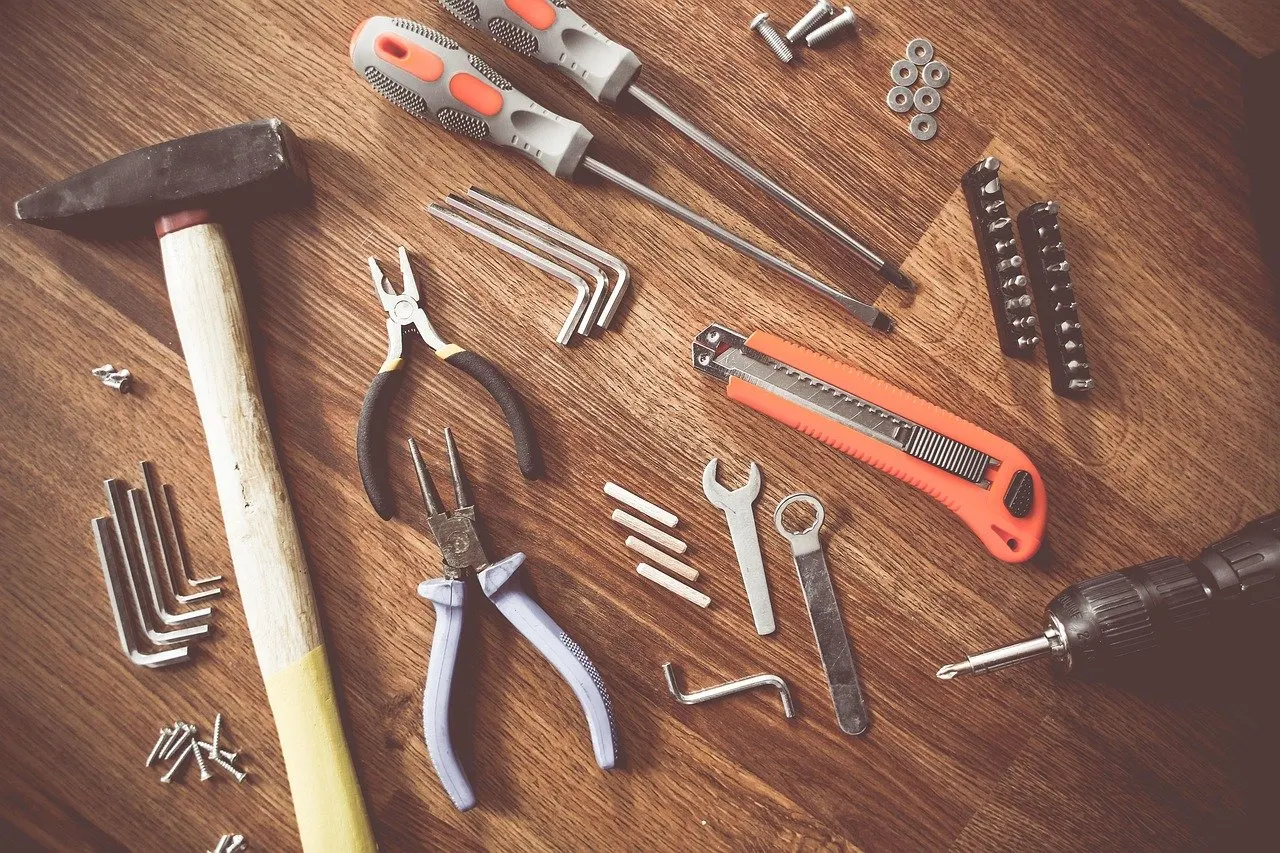 Verschiedene Handwerkzeuge wie Hammer, Zangen, Schraubendreher, Inbusschlüssel und Cutter liegen auf einer Holzoberfläche.