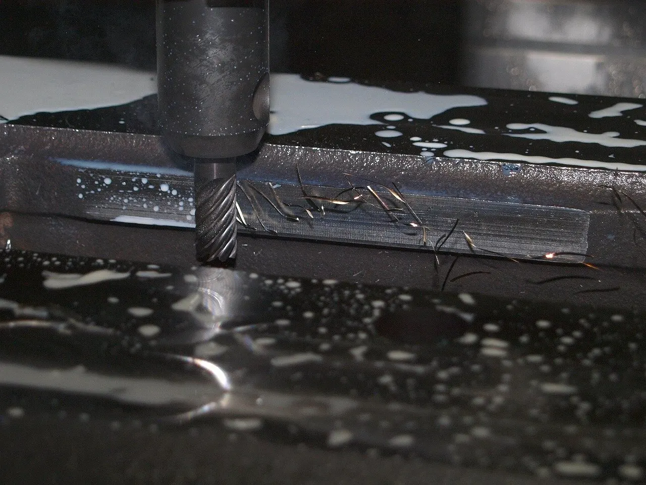 Schaftfräser taucht in ein Metallwerkstück ein, Kühlmittel benetzt die Oberfläche, Späne liegen auf dem Werkstück.
