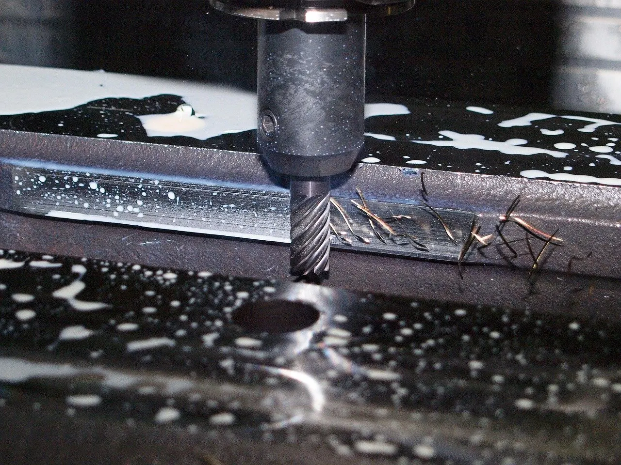 Schaftfräser in einer Maschine fräst eine Metallnut unter Kühlmittelzufuhr, Späne liegen auf dem Werkstück.