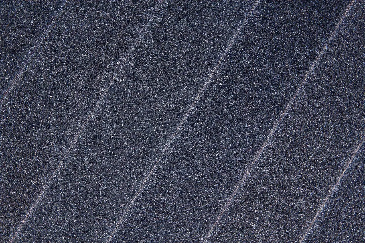 Dunkelgraue Schleiffläche mit feiner Körnung und hellen Rillen in diagonaler Anordnung.