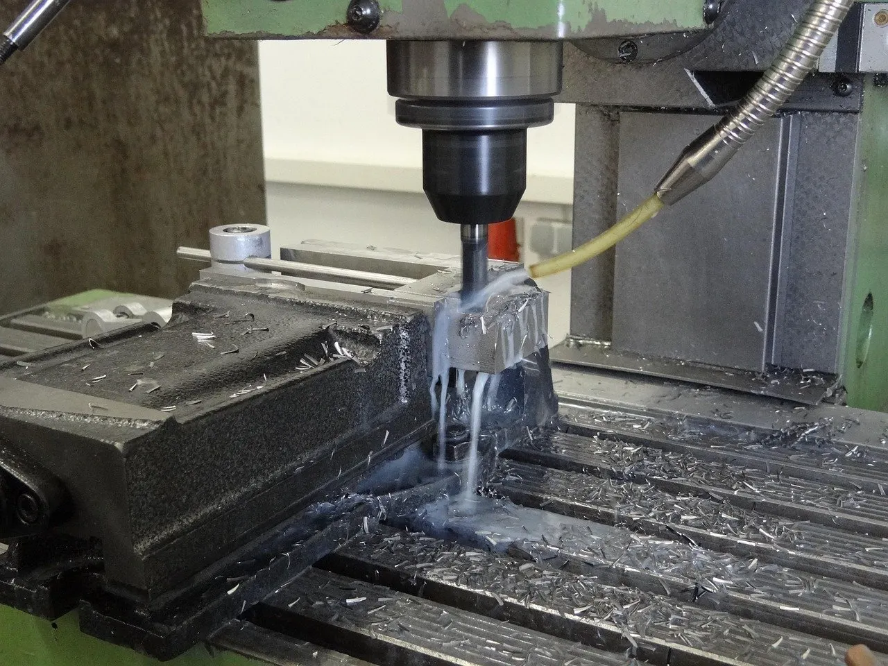 Fräskopf bearbeitet ein Werkstück in einem Maschinenschraubstock, Kühlmittel läuft über das Werkstück ab.