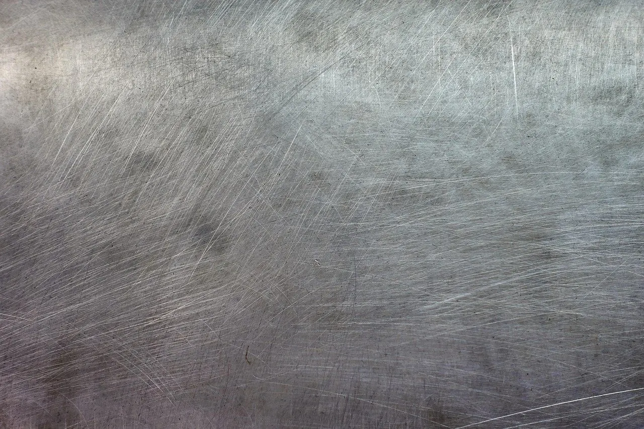 Grau-silbrige Metalloberfläche mit feinen Kratzspuren und Schleifriefen in diagonaler Richtung.